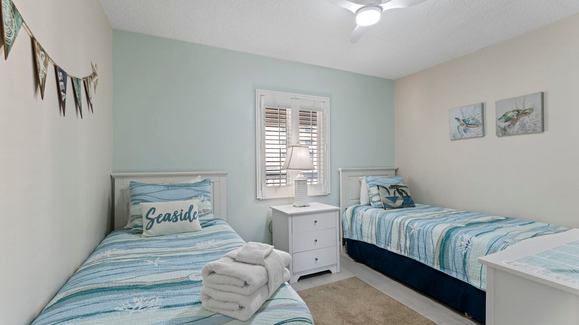 A bedroom with two beds, a nightstand, a lamp, and a window with blinds.