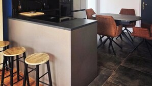 A modern kitchen with a central island, bar stools, and a dining area with chairs.