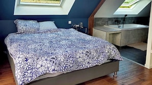 A bedroom with a skylight, a bed with a floral bedspread, and a view of a bathroom with a bathtub.