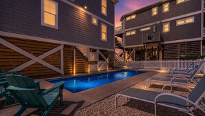 A swimming pool with lounge chairs and a wooden deck, surrounded by buildings with multiple windows and a white fence. - Experience ocean views at Panama Breeze, a spacious 6-bedroom retreat in Oak Island. (Oak Island)