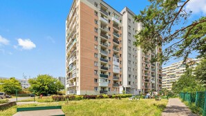 A multi-story residential building with balconies, a green fence, and a clear sky. - RentPlanet - Apartament Przymorze (Gdańsk)