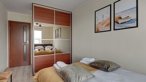 A hotel room with a bed, a wooden wardrobe, and two framed pictures on the wall. - RentPlanet - Apartament Przymorze (Gdańsk)