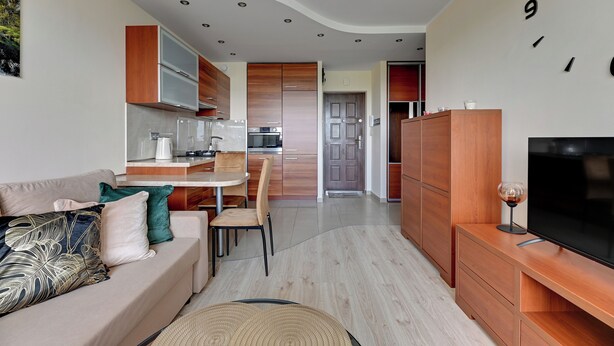 A modern living room with a sofa, TV, and wooden cabinets. - RentPlanet - Apartament Przymorze (Gdańsk)