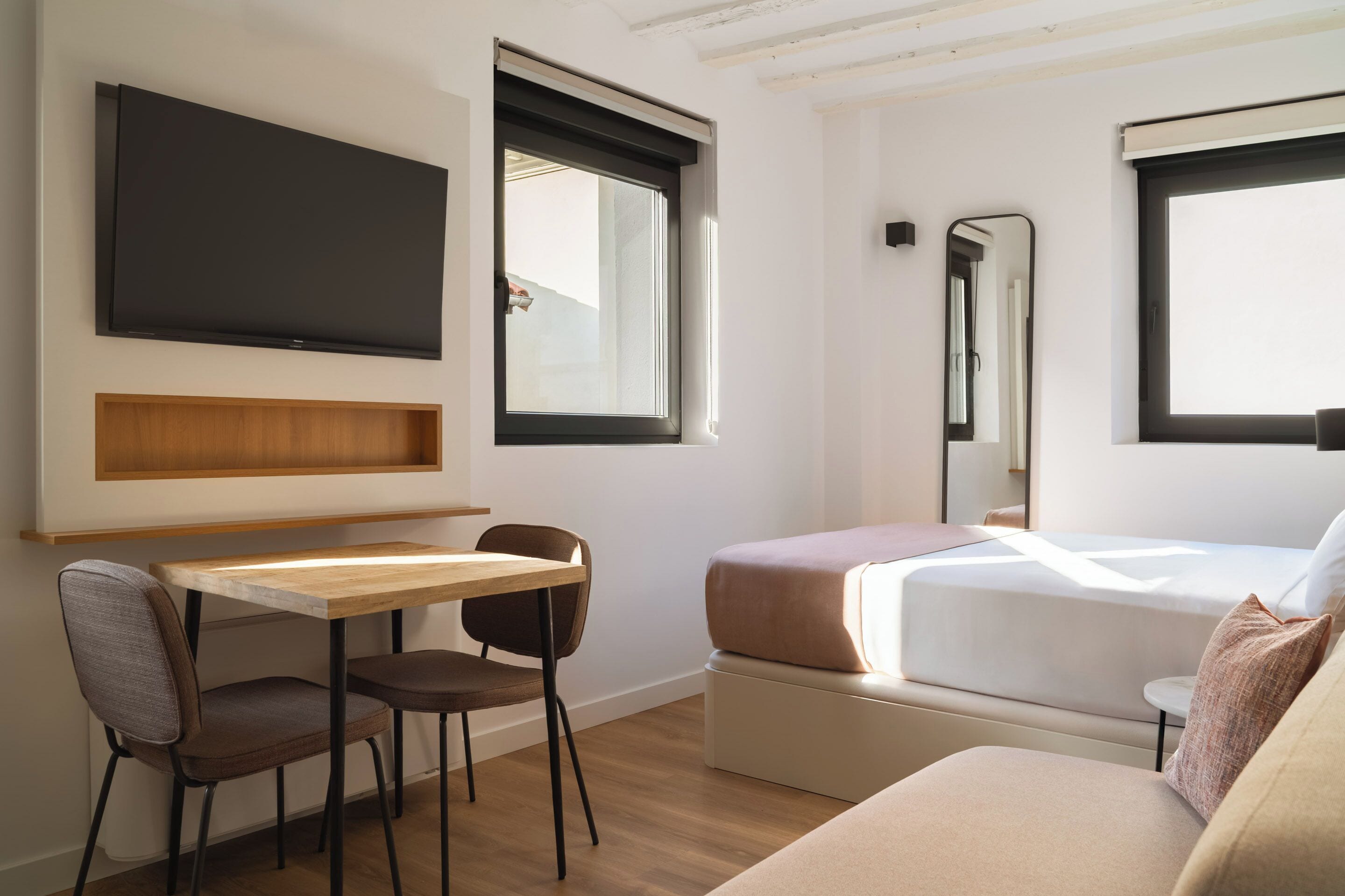 Una habitación de hotel moderna con una cama, un escritorio, una silla, un televisor y una ventana.