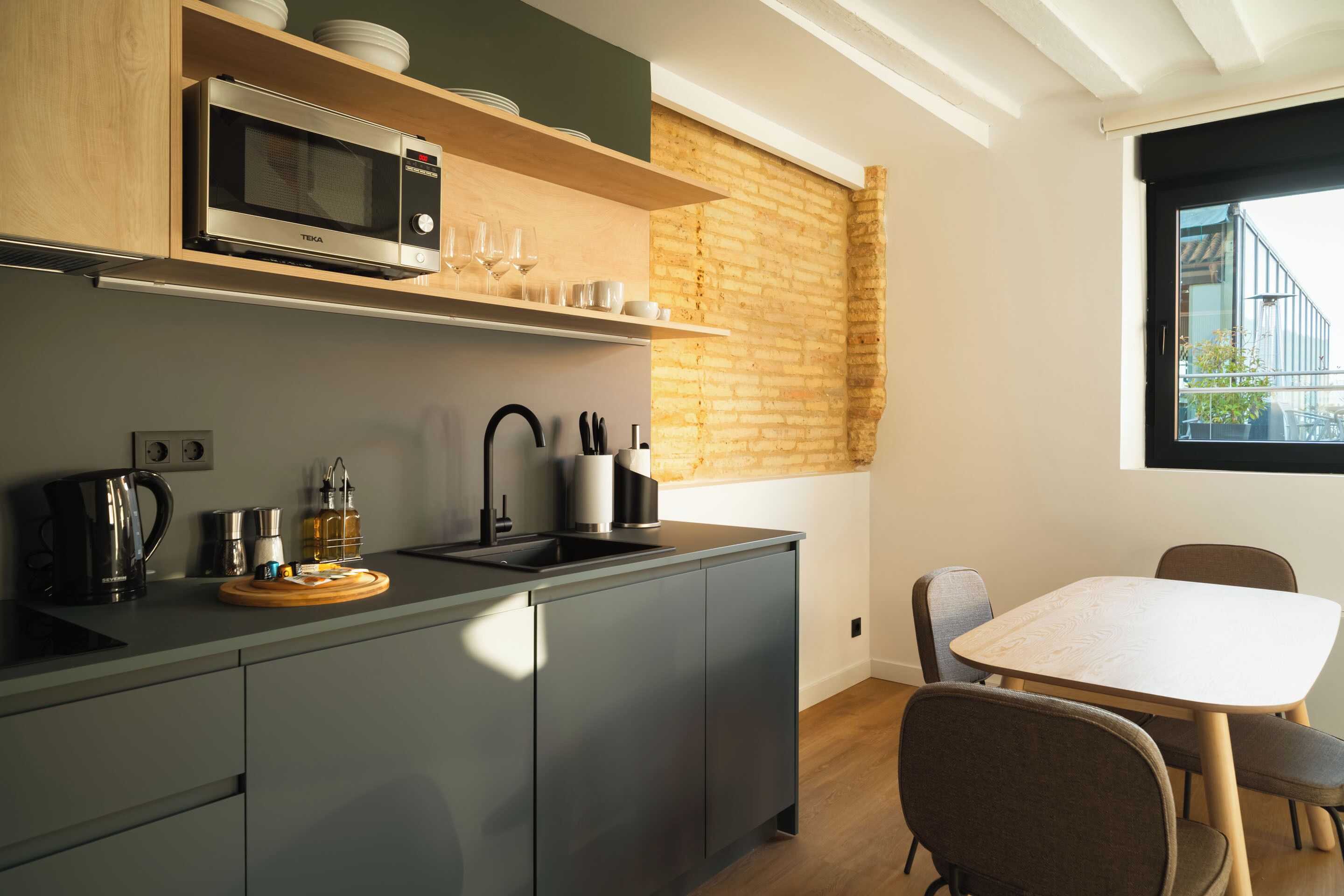 Una cocina moderna equipada con microondas, hervidor de agua y cafetera. Hay una mesa de comedor con sillas y una ventana con vistas a un edificio.