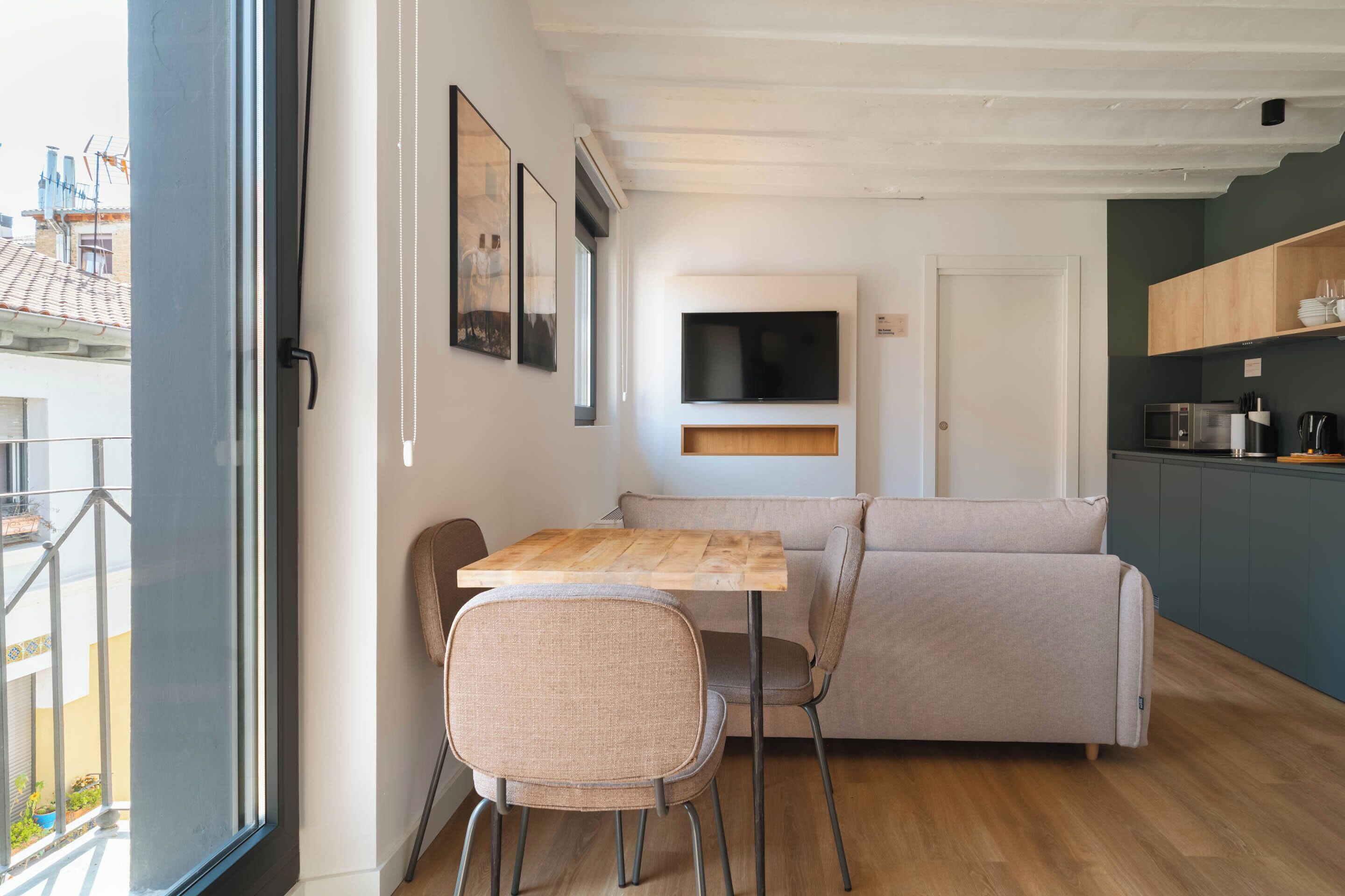 A modern living room with a sofa, a wooden table, and a TV mounted on the wall.