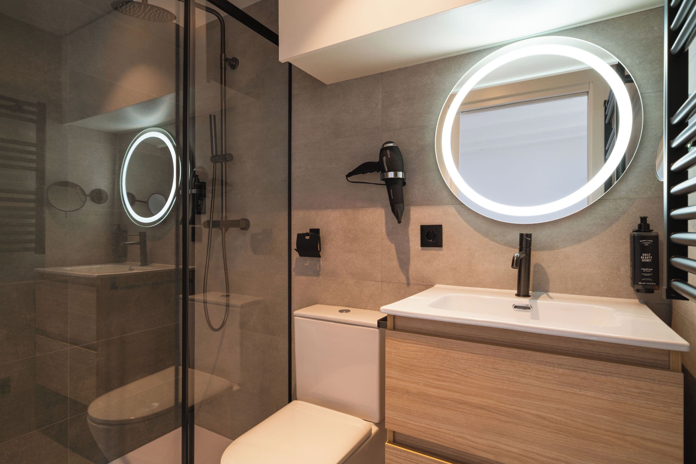 Un baño moderno con ducha de vidrio, inodoro, lavabo con espejo y un perchero para toallas.