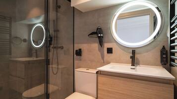 Un bany modern amb dutxa de vidre, un vàter, un lavabo amb mirall i un suport per a tovalloles.