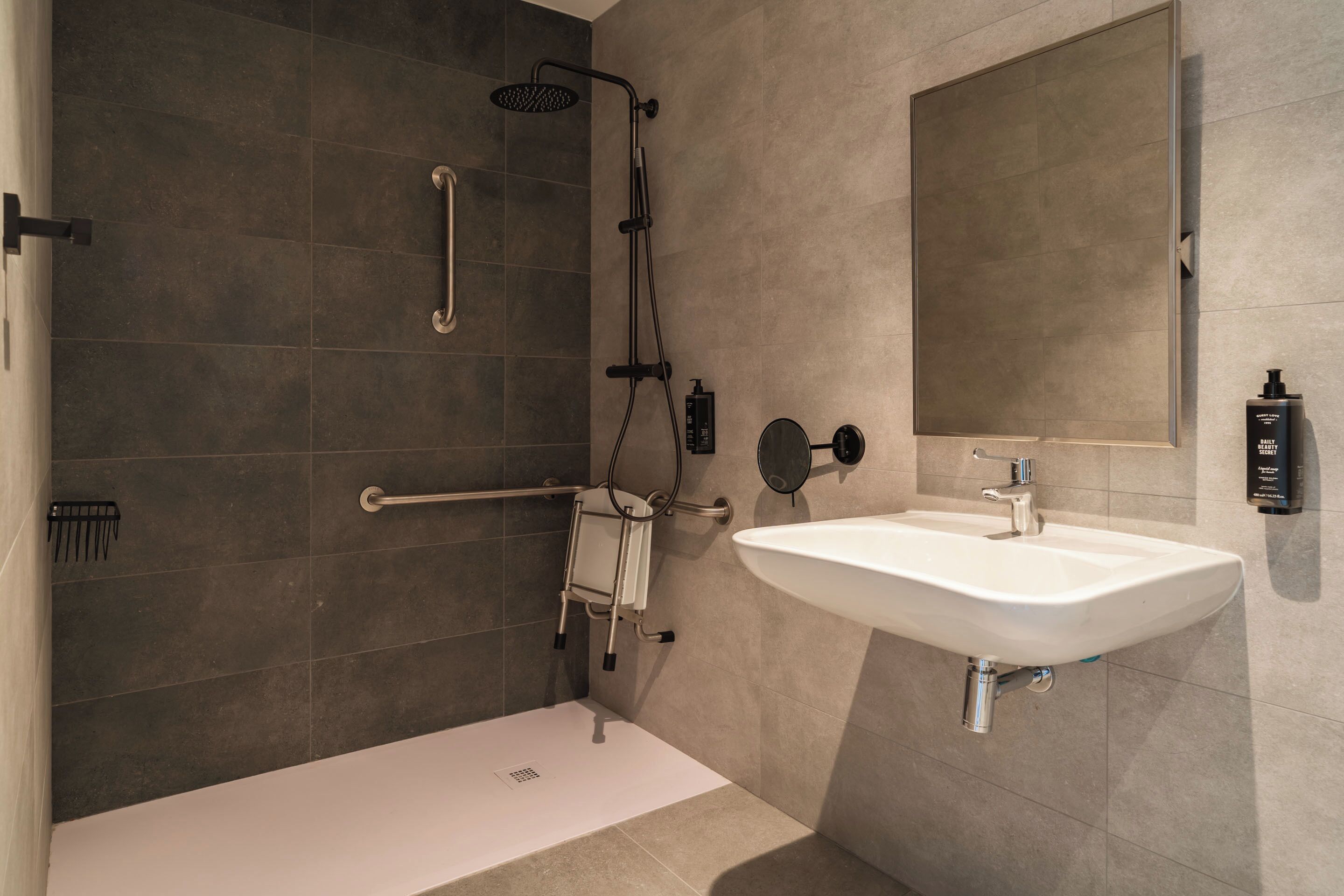 A modern bathroom with a shower, a white sink, and a large mirror.