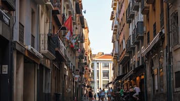 A narrow street flanked by multi-story buildings with balconies and outdoor seating areas.