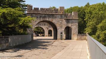 A stone bridge with arched passageways and a metal railing, surrounded by trees.