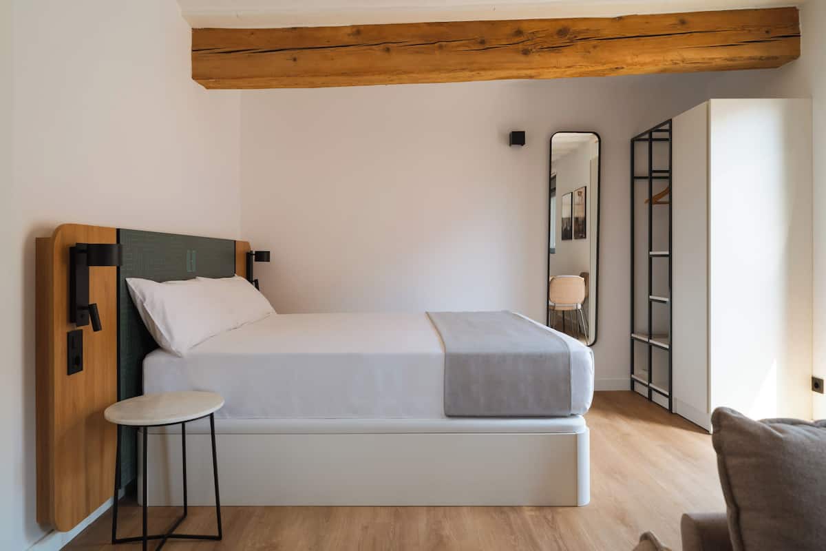 Quarto moderno com cabeceira de madeira, uma cama de solteiro, um banquinho pequeno, mesa de cabeceira e guarda-roupa com espelho.