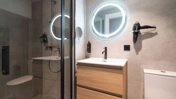 Une salle de bain moderne dotée d’une douche à parois de verre, d’un meuble-lavabo avec un miroir et d’un sèche-cheveux fixé au mur.