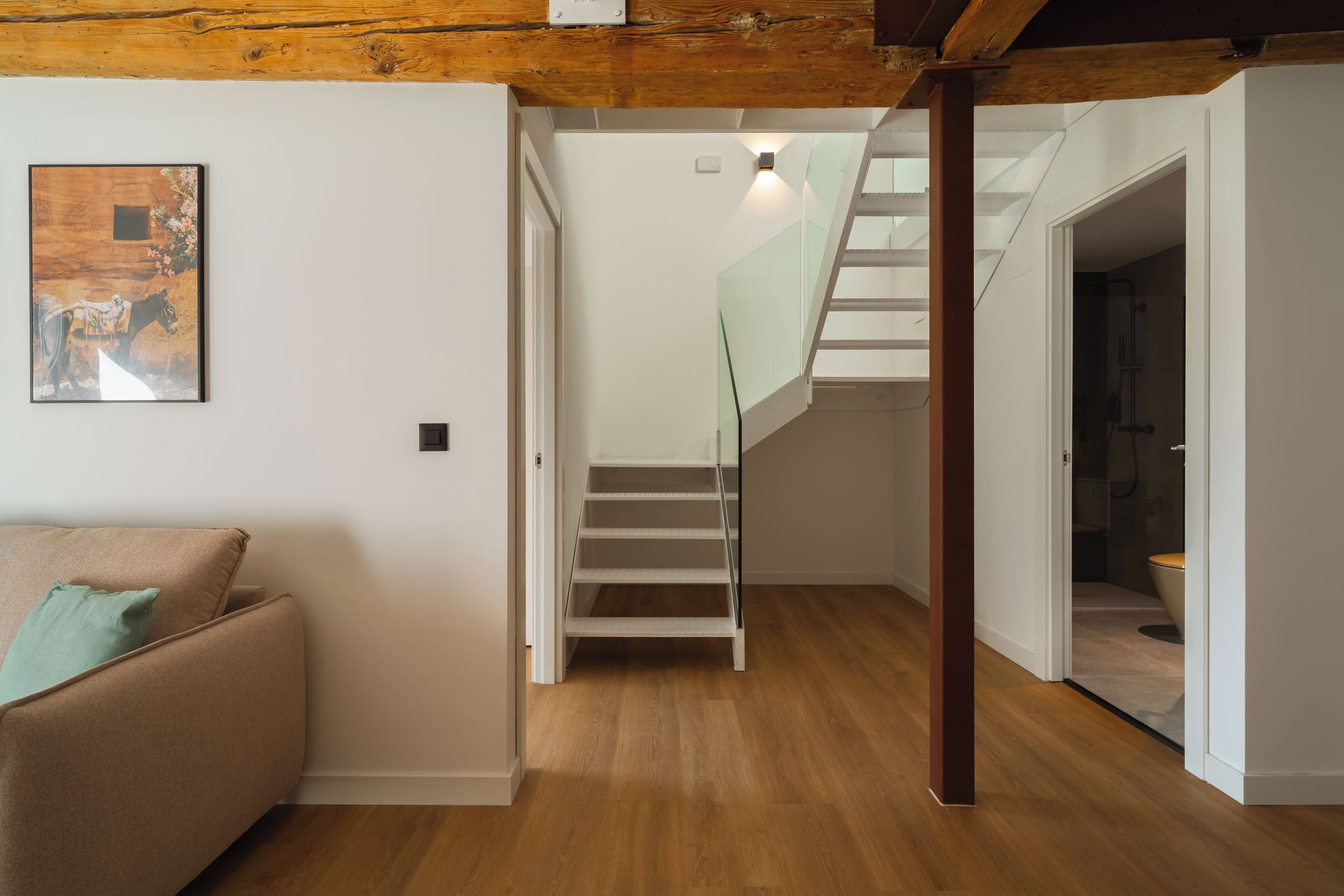 A modern interior with a staircase leading to a second floor, a wooden ceiling, and a framed picture on the wall.