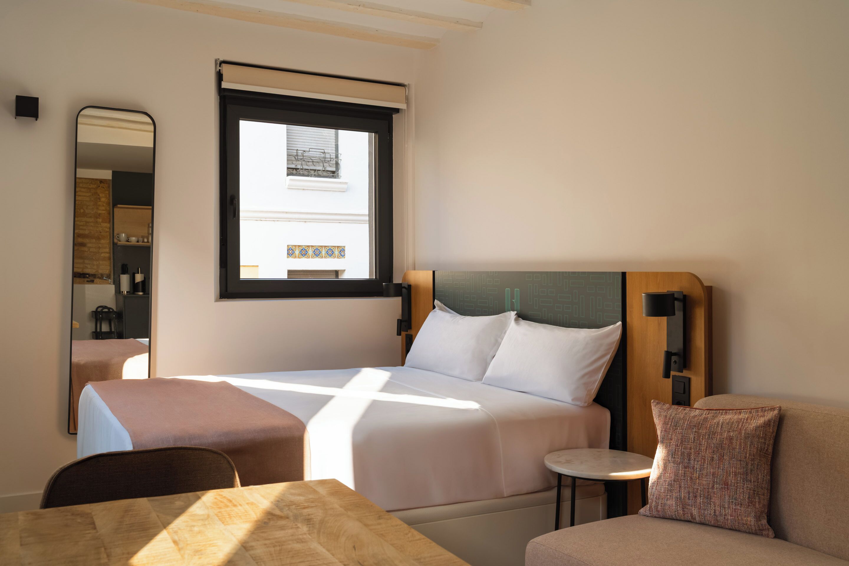 Ein Hotelzimmer mit Bett, kleinem Tisch, Stuhl, Sofa, Spiegel und Fenster.