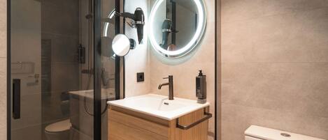 Une salle de bain moderne avec une douche à parois de verre, un meuble-lavabo avec un placard en bois, un miroir rond avec un éclairage intégré et des toilettes.