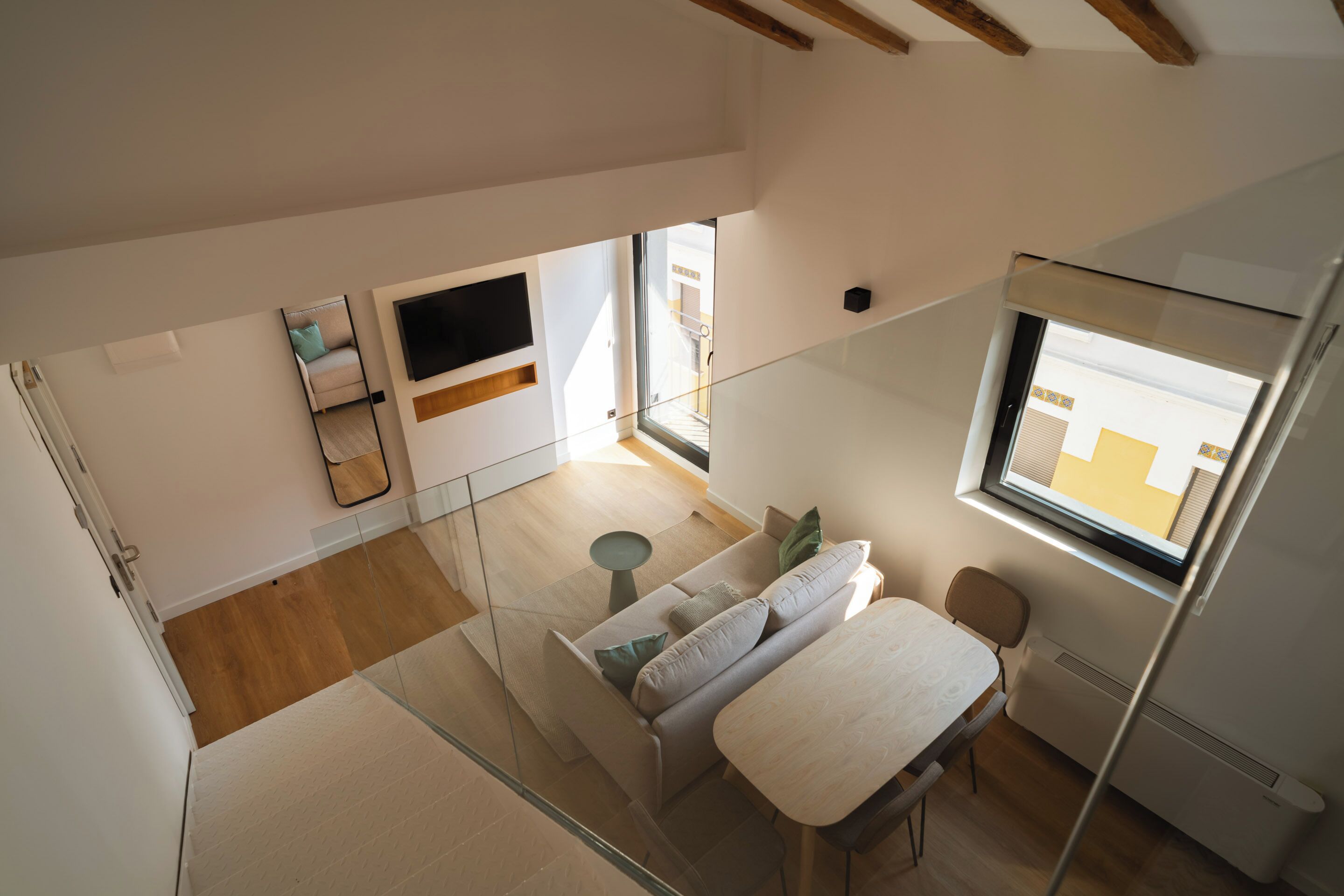 A modern, well-lit room with a glass partition, a sofa, a small table, and a TV mounted on the wall.