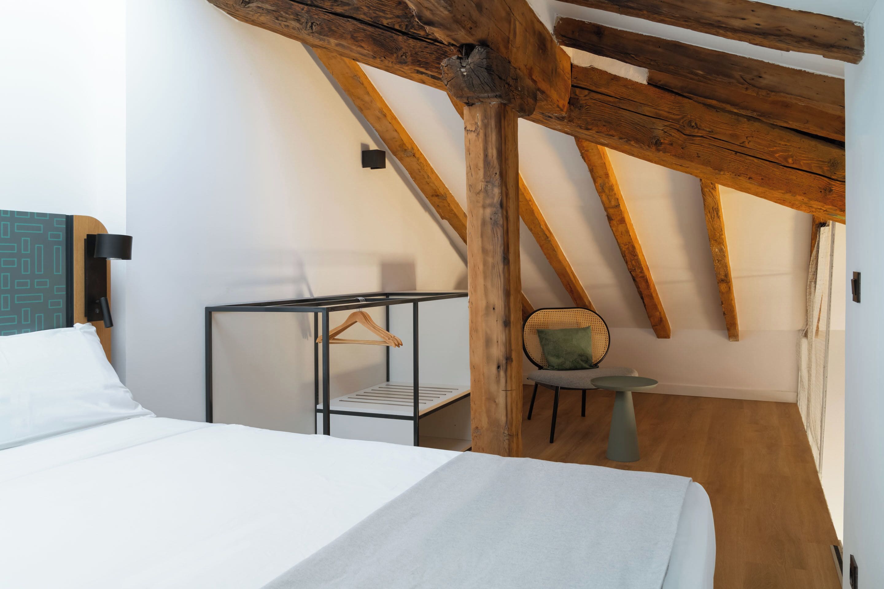 Une chambre à coucher comprenant un lit, une chaise, une petite table et un porte-vêtements suspendu.