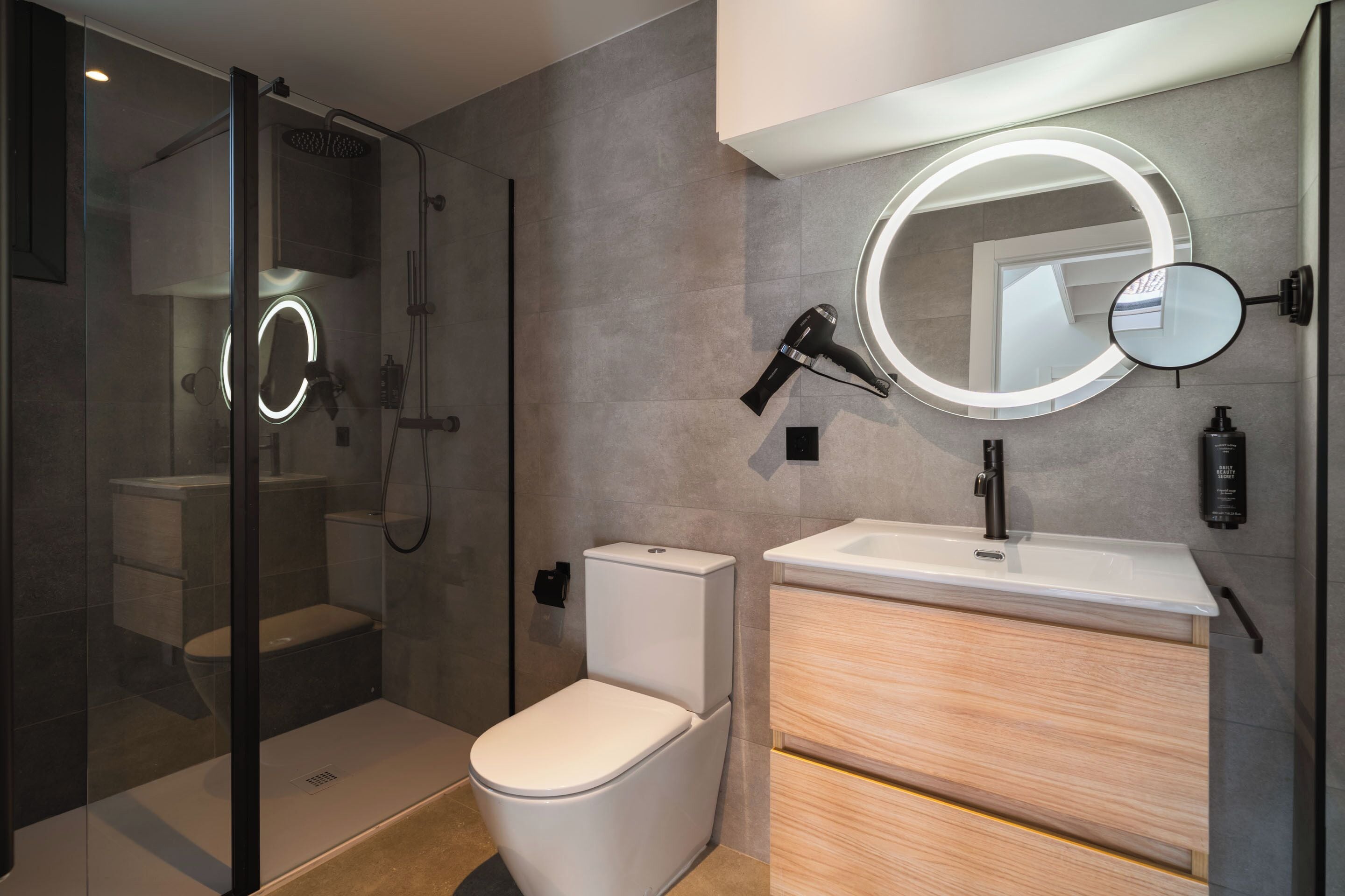 Un baño moderno con ducha envuelta en vidrio, inodoro y tocador con espejo y lavamanos.