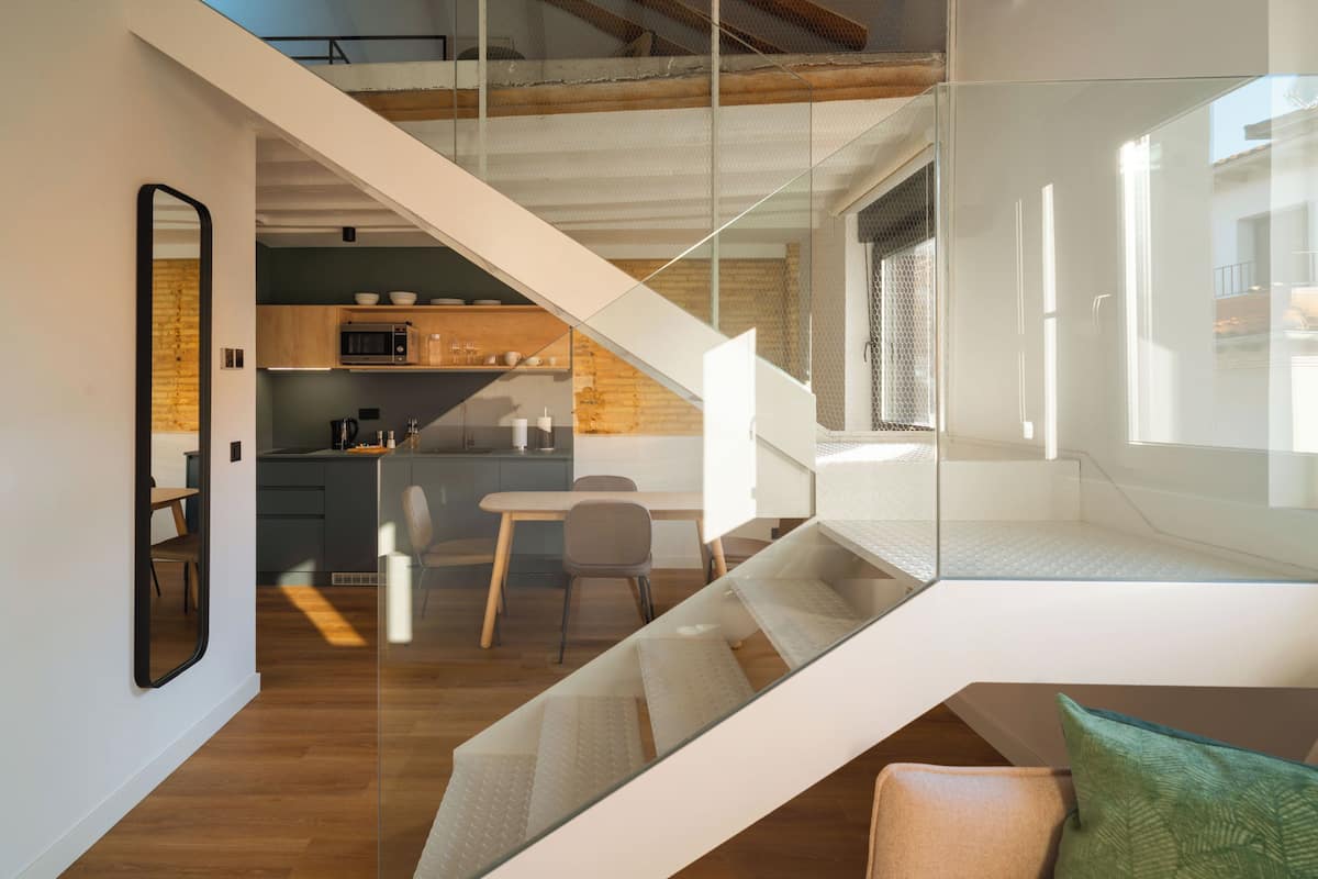 Um interior moderno com escadas que levam a um quarto no loft, uma área de refeições e uma cozinha com armários de madeira e micro-ondas.