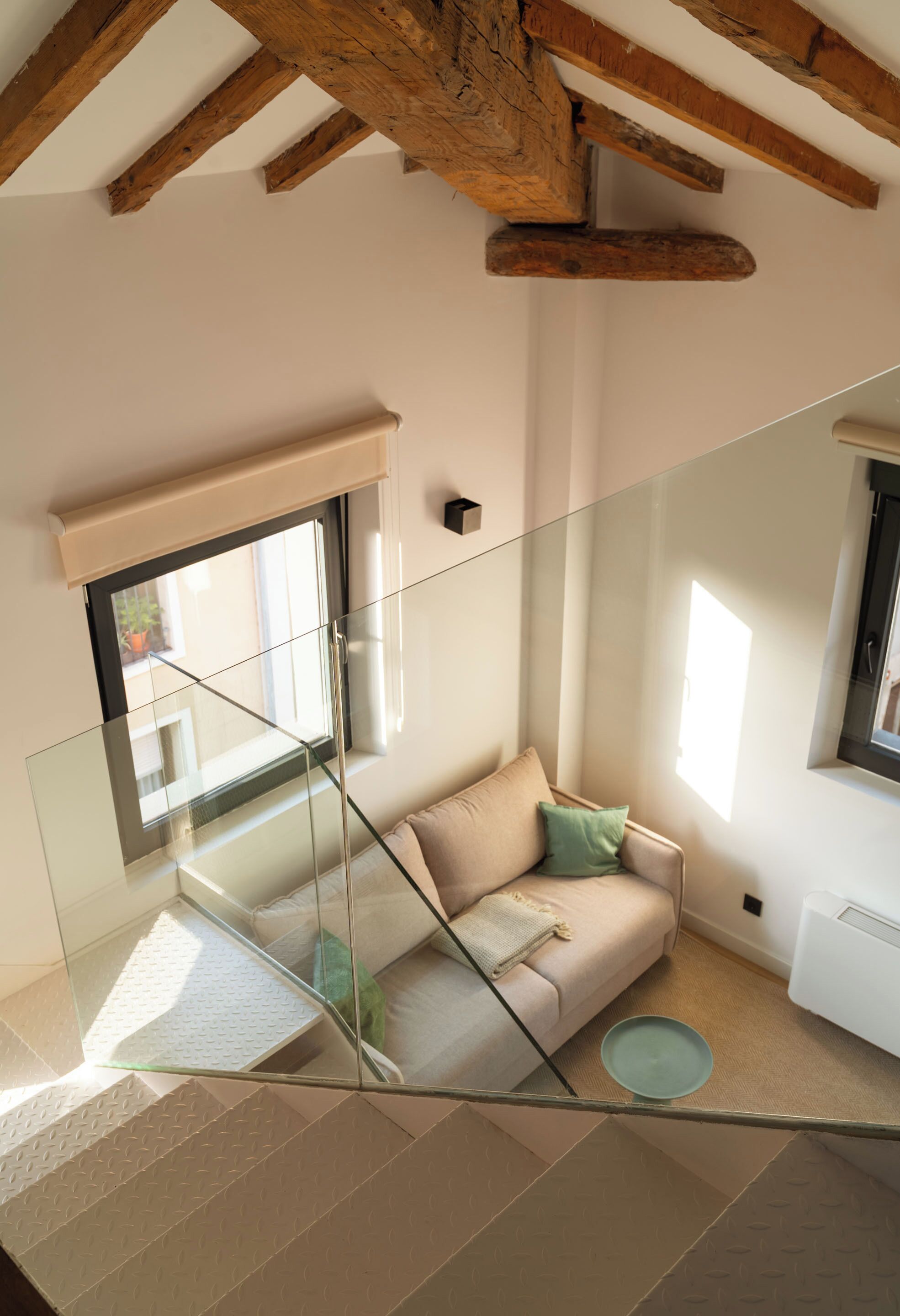 Un soggiorno moderno con una scala in vetro, un divano beige e un piccolo tavolino rotondo.