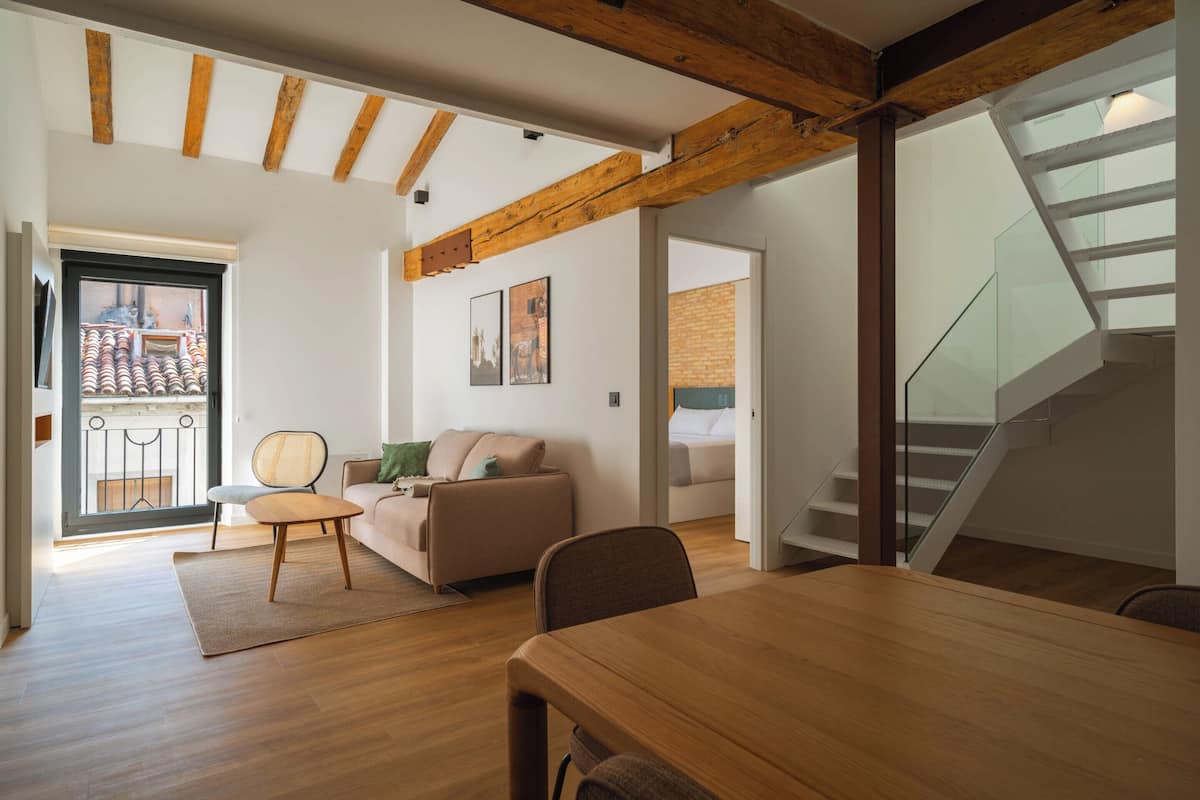 Uma sala de estar espaçosa com uma mesa de jantar de madeira, um sofá e uma escada.