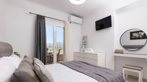Un dormitorio con cama, escritorio, silla, televisión y balcón con cortinas.