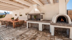 Un patio exterior con un horno de ladrillo, una mesa de comedor con sillas y una estructura de pérgola.