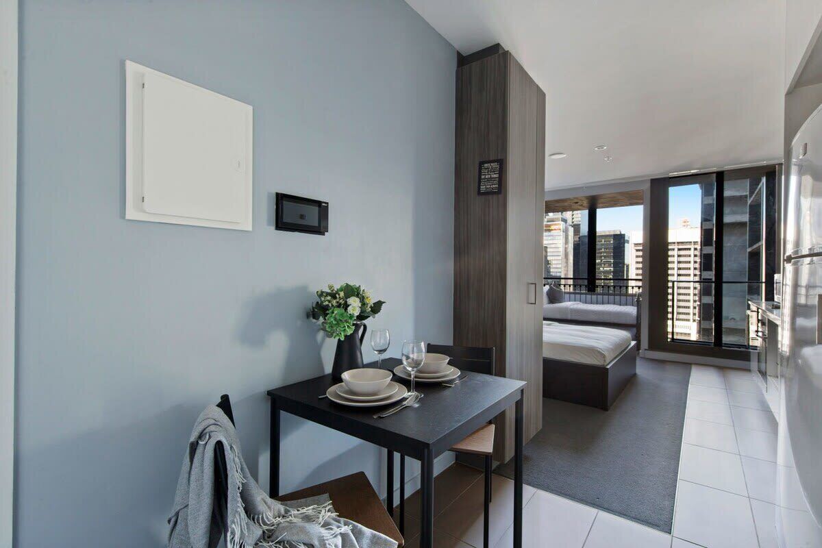 A modern hotel room with a dining area, a bed, and a view of the city.