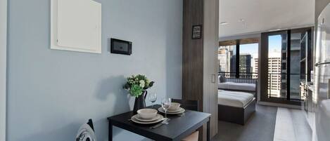 A modern hotel room with a dining area, a bed, and a view of the city.