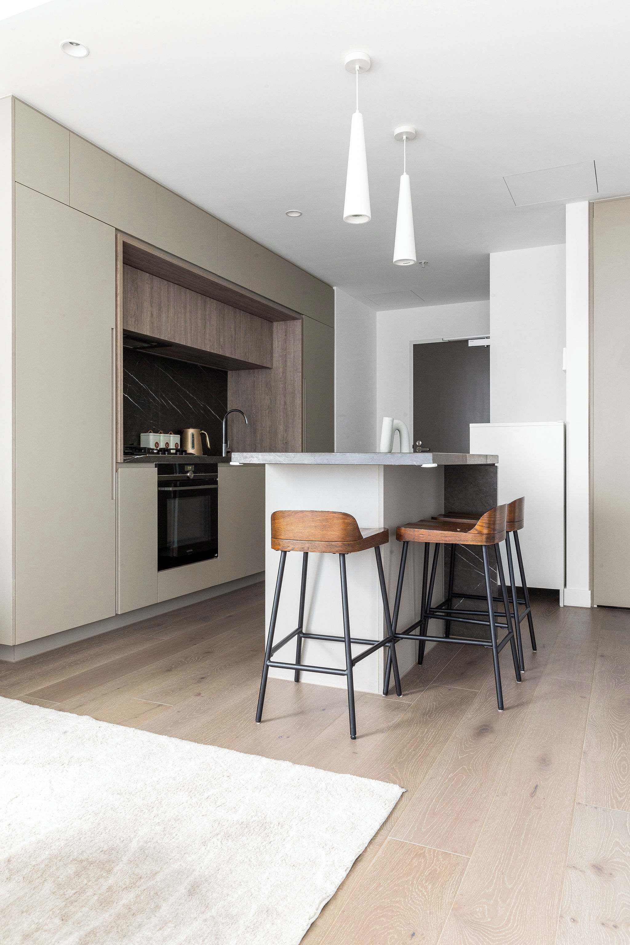 A modern kitchen with a built-in oven, a sink, and a bar area with stools.