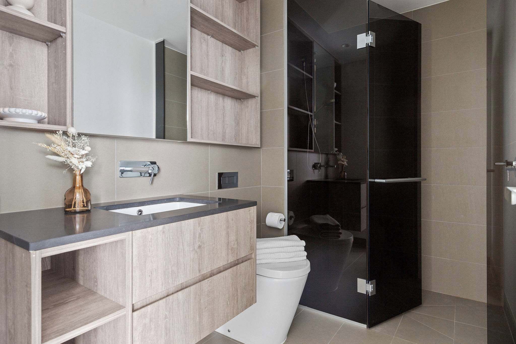 Een moderne badkamer met een houten wastafelmeubel, een douchecabine met glazen wanden en een wit toilet.