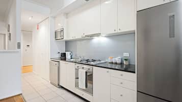 Uma cozinha moderna com armários brancos, eletrodomésticos de aço inoxidável e bancada preta.
