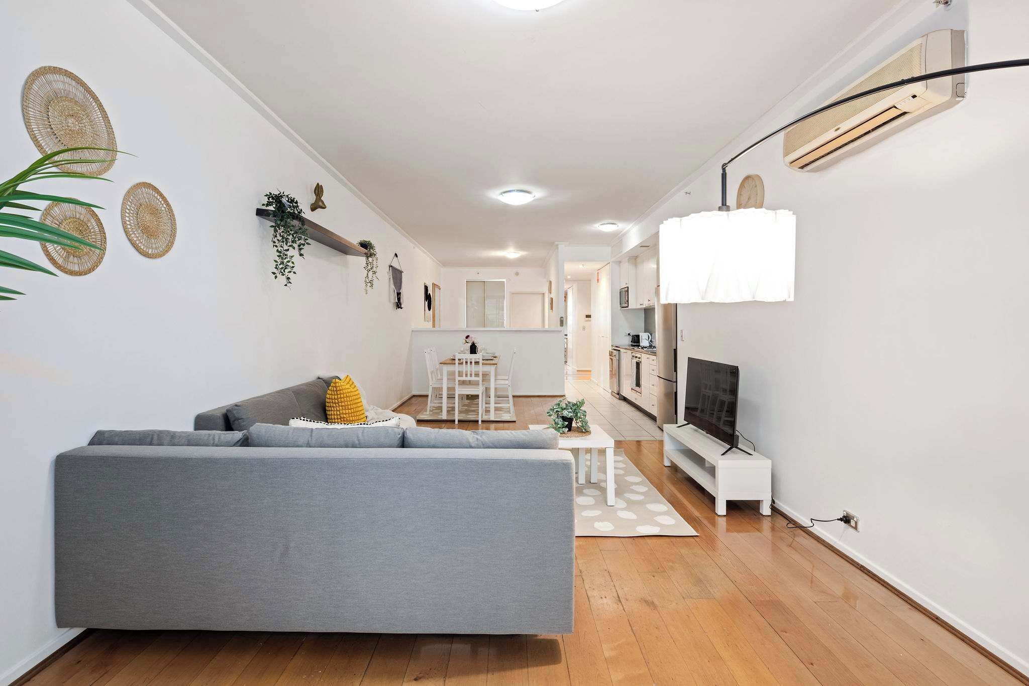 A modern living room with a grey sofa, a small white table, and a TV on a stand.