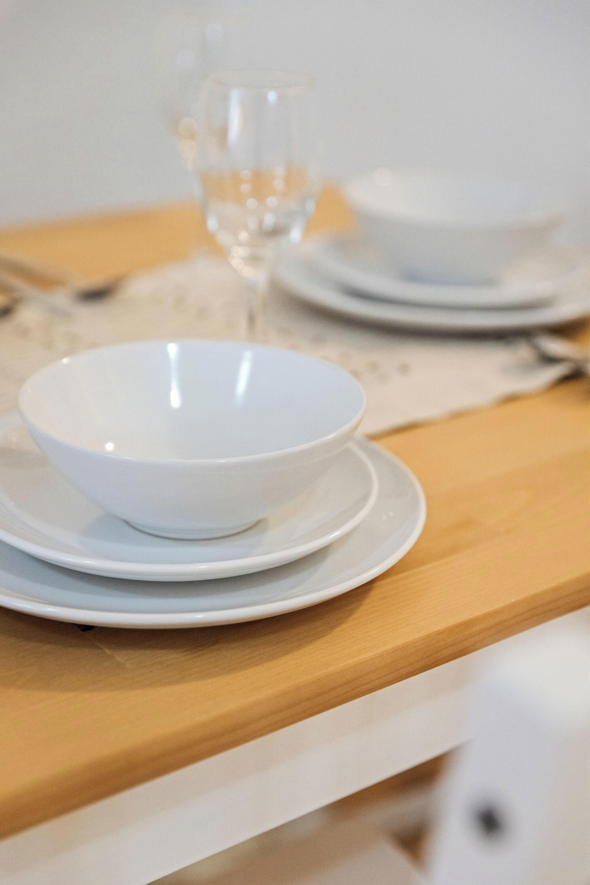 A dining table with a white bowl and plate set on a wooden surface.