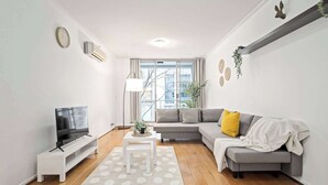A modern living room with a flat-screen TV on a white stand, a grey sofa with cushions, a small white table with a plant, and a large polka dot rug. - A Stylish Studio for 6, Next to Darling Harbour (Sydney)