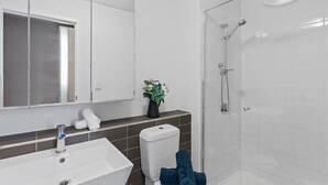 A modern bathroom with a white sink, a glass shower enclosure, and a mirror above the sink. - City-view Studio Near Southern Cross (Melbourne)