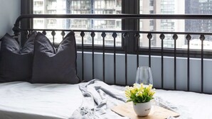 A balcony with a view of city buildings, a bed with pillows, a glass of water, and a potted plant. - City-view Studio Near Southern Cross (Melbourne)