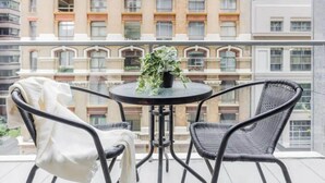A balcony with two wicker chairs and a small table, a potted plant on the table, and a view of a multi-story building with balconies. - Spacious & Comfy Apt for 6 Next to Darling Harbour (Sydney)