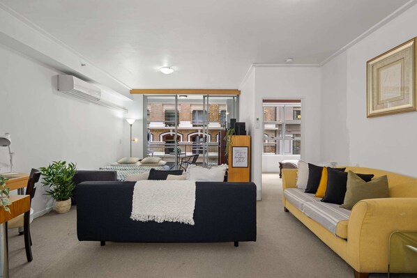A modern living room with a black sofa, a yellow sofa, and a dining area with a table and chairs. - Spacious & Comfy Apt for 6 Next to Darling Harbour (Sydney)