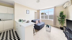 A compact living space with a kitchenette, a sofa, a TV, and a potted plant. - A Comfy & Cozy Apt in Clifton Hill, Free Parking (Melbourne)
