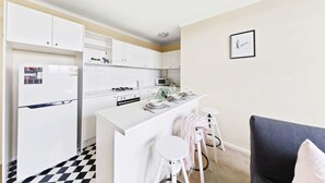 A modern kitchen with white cabinetry, a central island with stools, a microwave, and a refrigerator. - A Comfy & Cozy Apt in Clifton Hill, Free Parking (Melbourne)