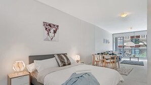 Une chambre moderne avec un grand lit, des tables de chevet, un bureau et une vue sur l’extérieur.