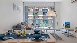 Un salon moderne avec un coin repas, de grandes fenêtres et une vue sur un immeuble à la façade en briques.