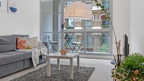 Un salon moderne avec un canapé gris, une table basse blanche et une grande fenêtre donnant sur un paysage urbain.