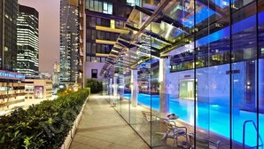 A modern hotel with a glass-enclosed infinity pool, a rooftop terrace, and a city view.
