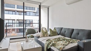 Ein modernes Wohnzimmer mit einem grauen Sofa, einem weißen Couchtisch und einem großen Fenster mit Blick auf ein Gebäude.