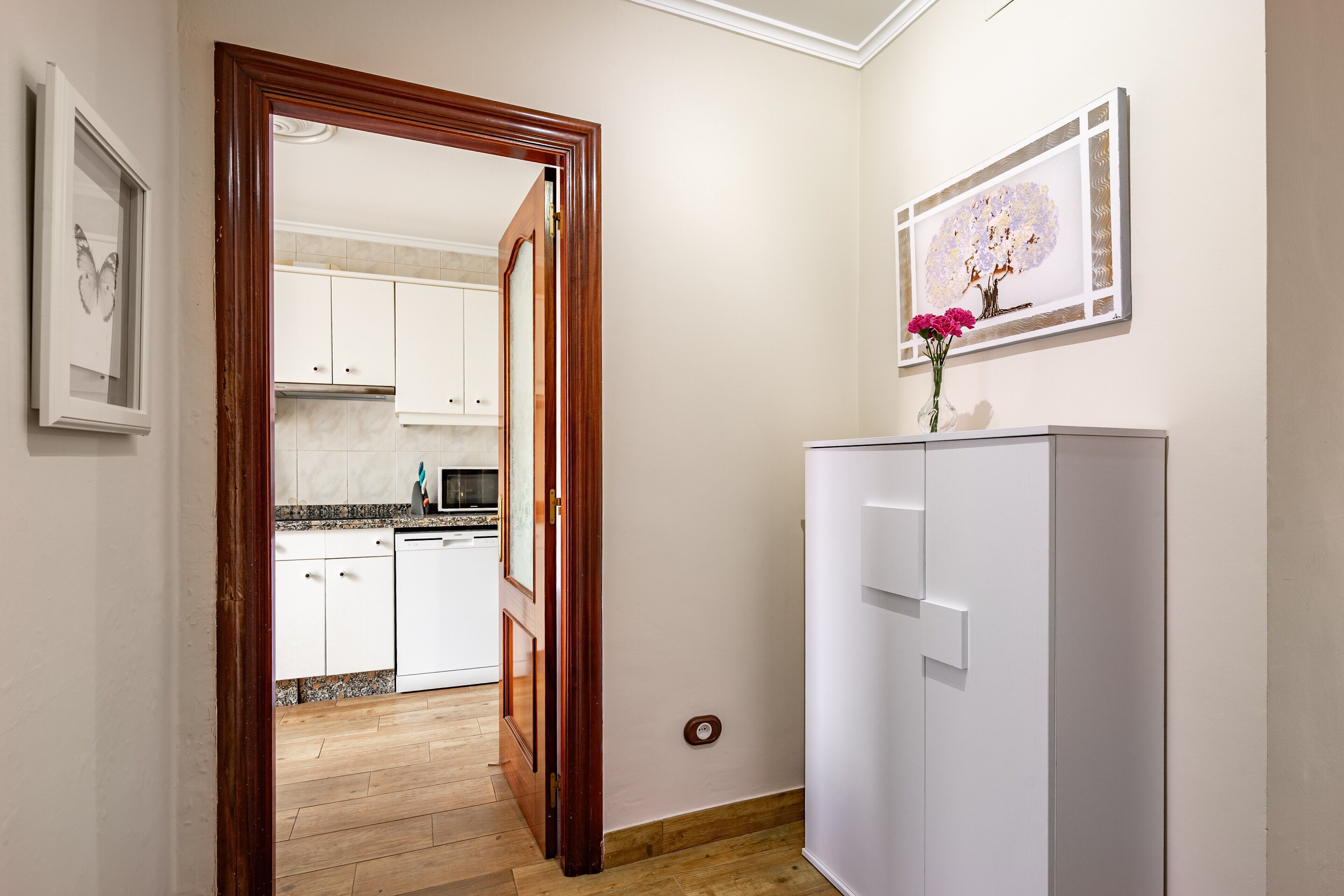 Un corridoio che conduce a una cucina con mobili bianchi, un frigorifero bianco e un quadro appeso al muro.