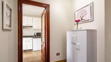 Un corridoio che conduce a una cucina con mobili bianchi, un frigorifero bianco e un quadro appeso al muro.