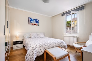 Une chambre à coucher comprenant un lit, une table de chevet, une chaise, une fenêtre et une œuvre d’art accrochée au mur.